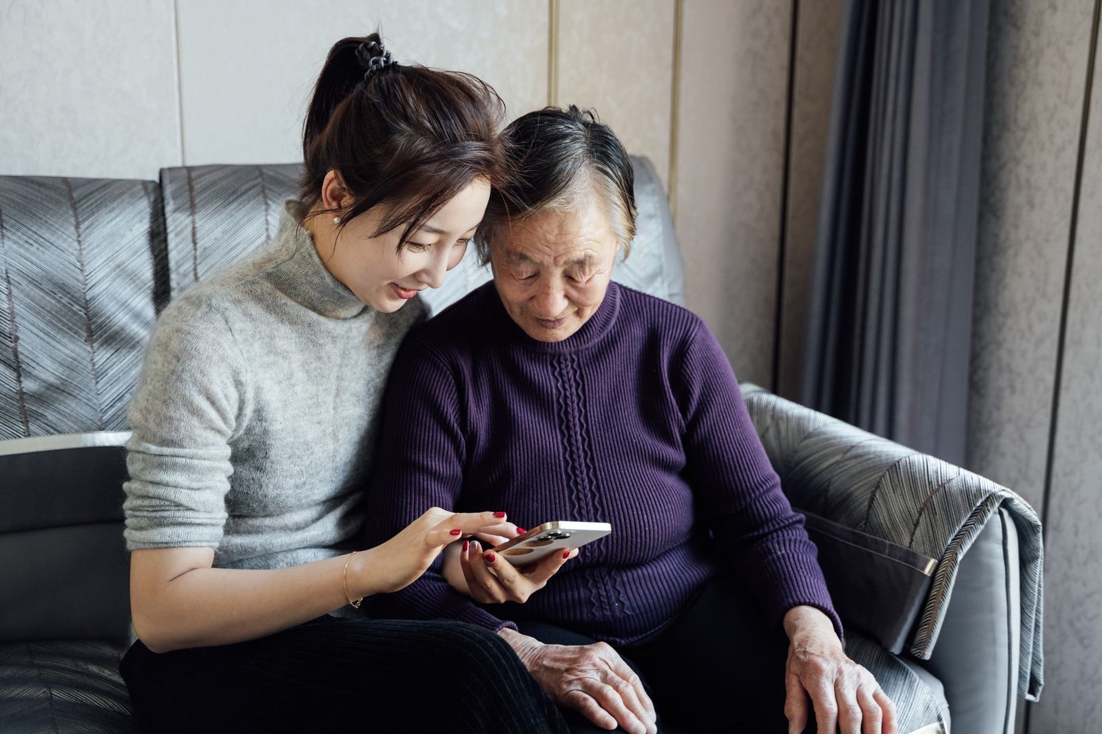 A daughter and her mother sitting together on a sofa, looking at a phone