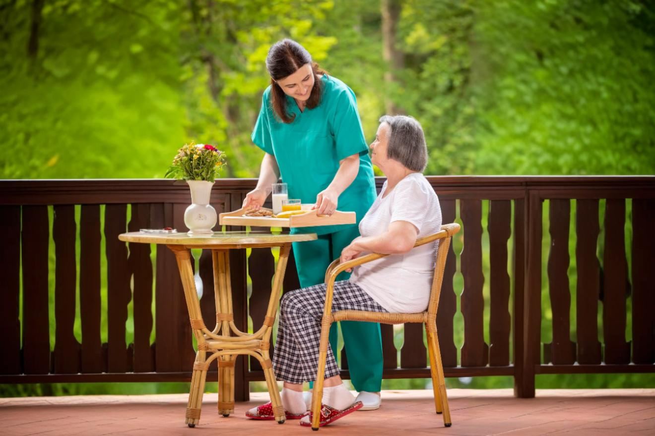 Caregiver serving breakfast to an older woman on an outdoor patio